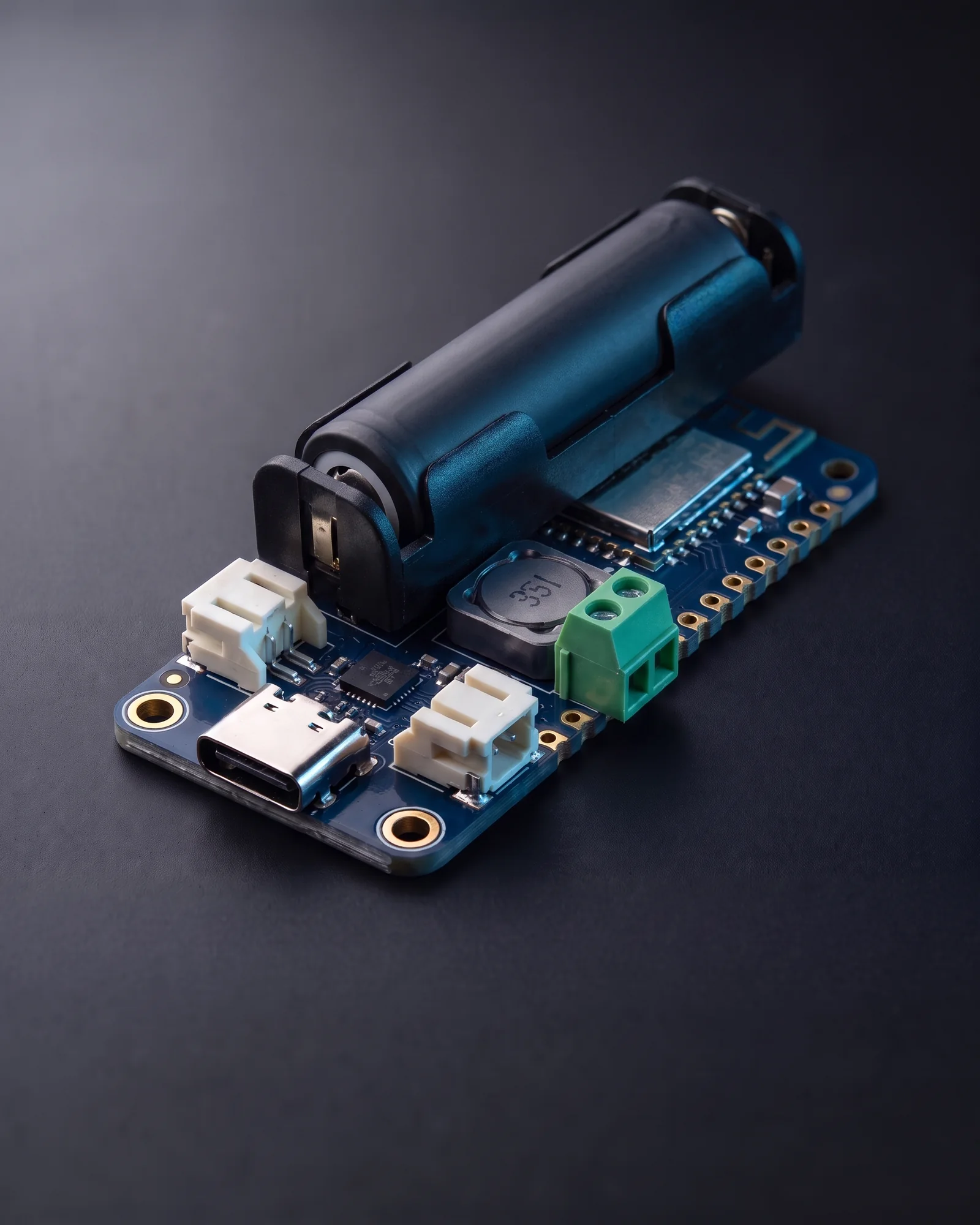 The Snowbird 18650: a longer Feather-width navy board with an on-board 18650 cell holder holding one unbranded cell, USB-C and connectors at one end and the Bluetooth module at the other.