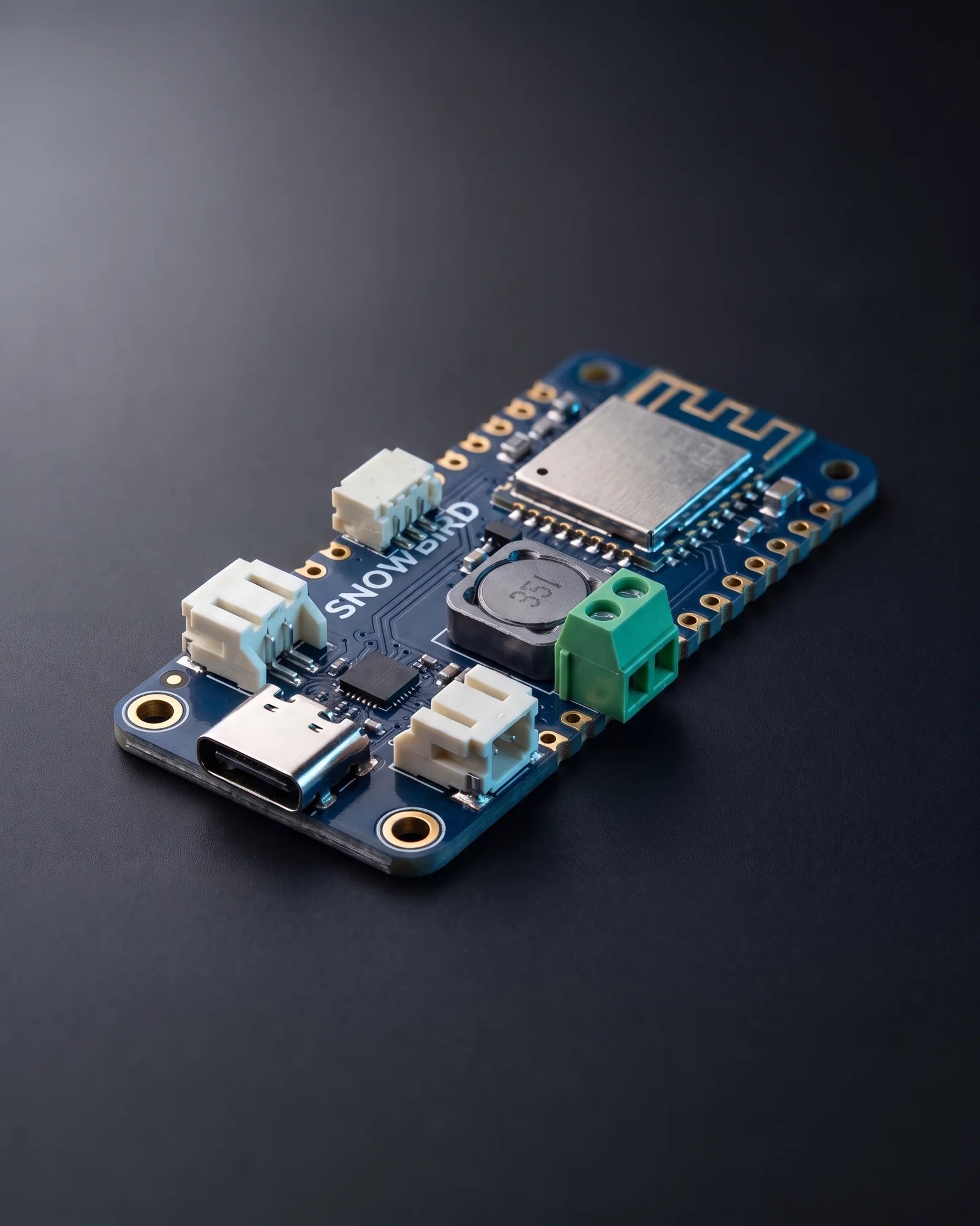 The Snowbird Feather 1S: a matte navy Feather-sized circuit board with gold castellated edges, a USB-C port, white JST connectors, a shielded Bluetooth module with a chip antenna, a power inductor and the Snowbird wordmark in white silkscreen.